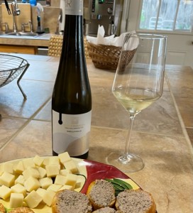 bottle of wine, glass of wine, cheese plate on counter.