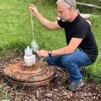 man stooping on ground and dipping wine from an in-ground amphora